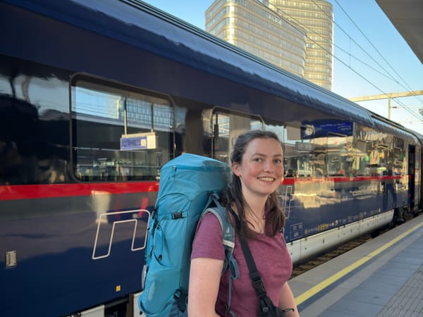 Karina steht mit Wanderrucksack am Bahnsteig. Hinter ihr steht ein Nightjet.